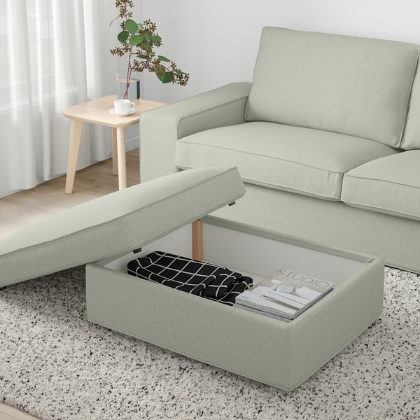 Green KIVIK footstool open with magazine organiser on rug near table with vase and cups.
