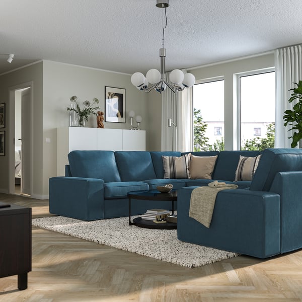 Modern living room: large blue KIVIK sofa with soft cushions, stylish coffee table, light wood floor, and large windows.
