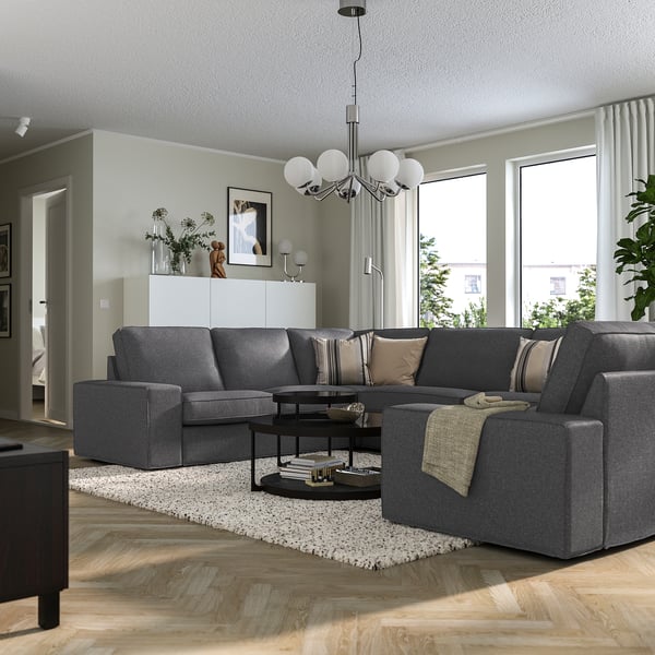 Modern living room with grey KIVIK sofa, natural light, coffee table, books, rug, and pendant light.