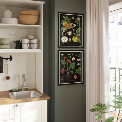 KNOPPÄNG prints with fruit art hang above kitchen sink, adding vibrant colour to dark green wall.