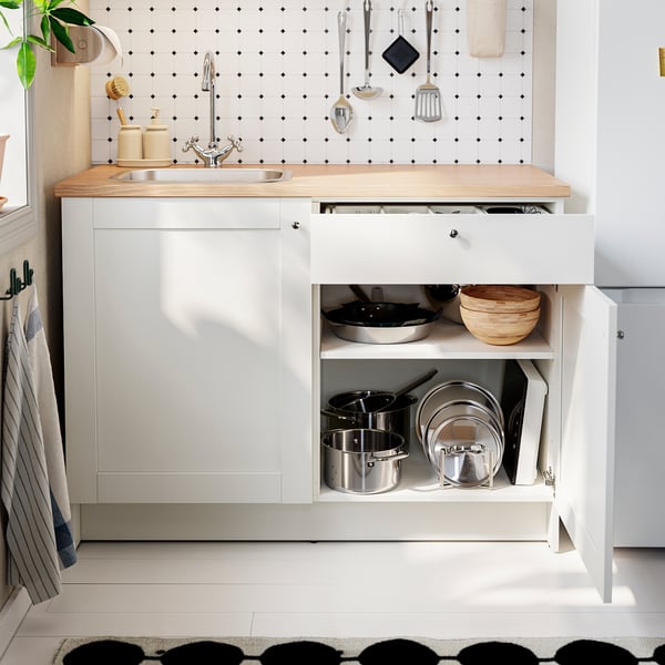 Modern kitchen, sliding cabinet open, showing pots and bowls, white cabinets with oak counter, black-and-white backsplash.