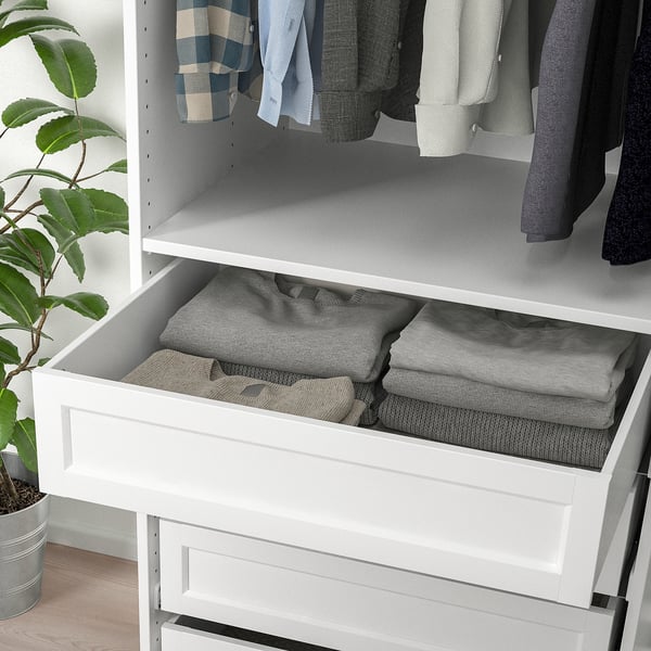 White pax drawer open, neatly folded grey clothes inside. Plant on wooden floor beside.