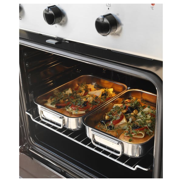 Two stainless steel trays with cooked food in an oven. Knobs on ovens white front.
