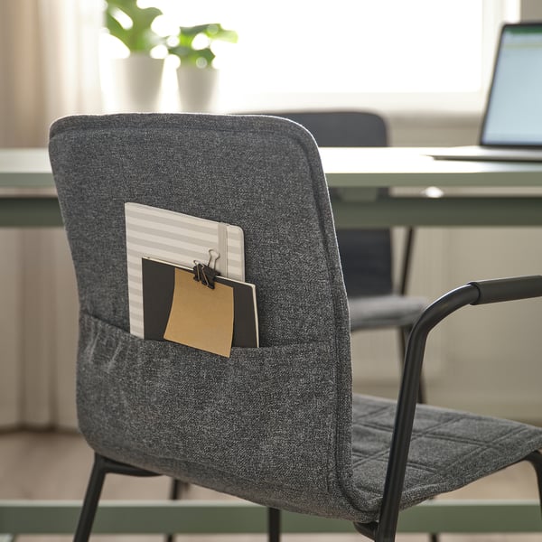 Grey office chair with cloth pocket holding notepad and paperclip, behind a desk with a laptop.