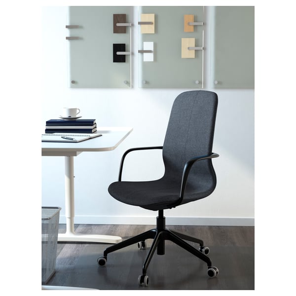 Modern office chair with height-adjustable seat, armrests, and lumbar support positioned near a white desk with a stack of books and a coffee cup.