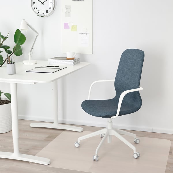 Modern minimalist home office. White desk, blue chair, white lamp, clock, plants, coffee cup, magazines.