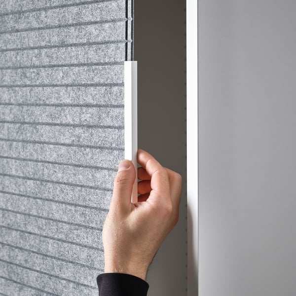 Hand adjusting white handle on grey felt panel. LARKOLLEN sliding door for platsa storage.