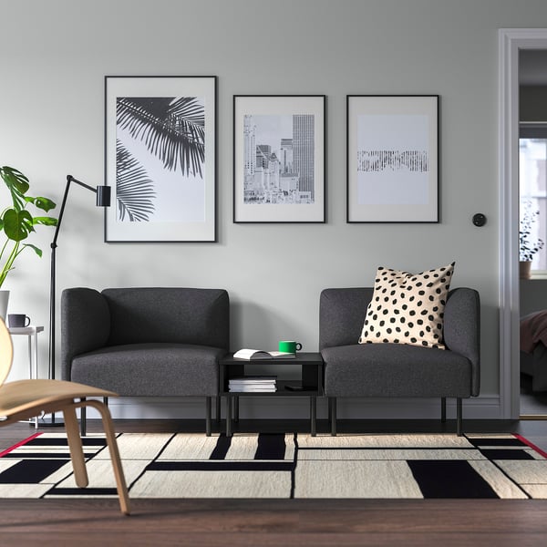 Minimalist living room with dark grey LILLEHEM sofa, black-and-white art, patterned rug, and green mug on small table.
