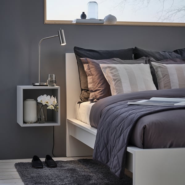 Modern grey MALM bed with striped pillows, black shoes on rug, wall lamp, and decor. Headboard reaches near ceiling, a focal point.