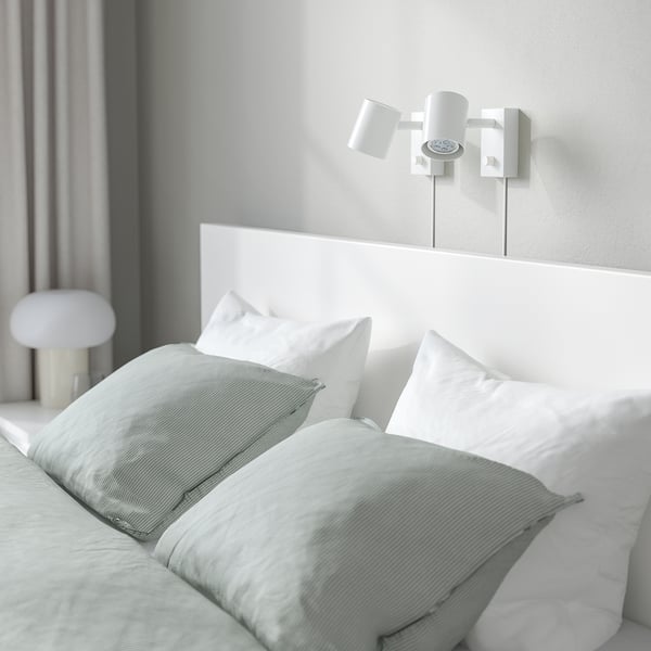 A modern bed with a white headboard, light green bedding, and wall-mounted bedside lamps, showcasing a clean and minimalist design.