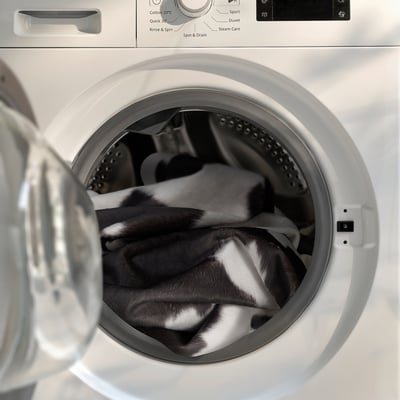 A white washing machine with a black and white cowhide-patterned rug inside, ready for washing.