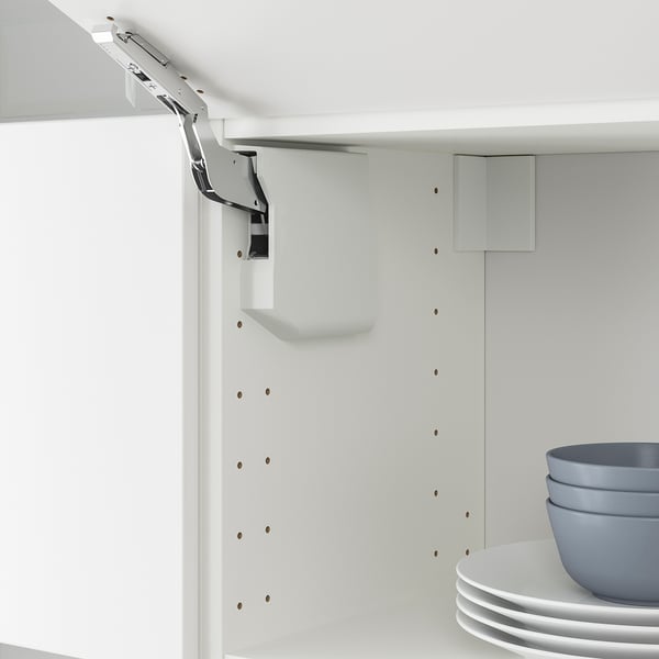 White kitchen cabinet with veddinge door lift mechanism shown, including catch for gentle closing. Stacked bowls and plates on shelf.