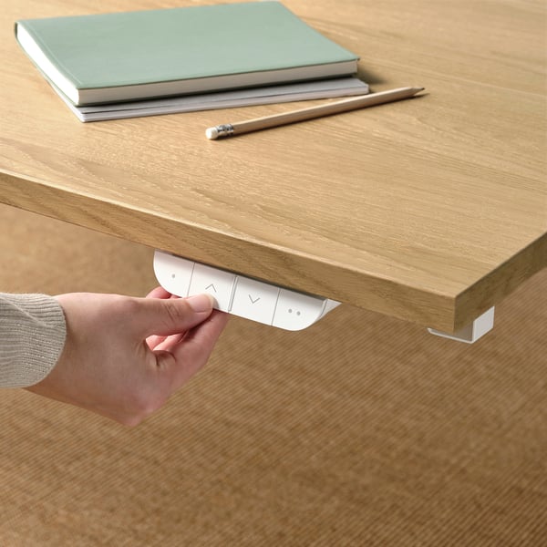 Hand adjusts electric sit/stand desks motor control, memory settings for height adjustment.