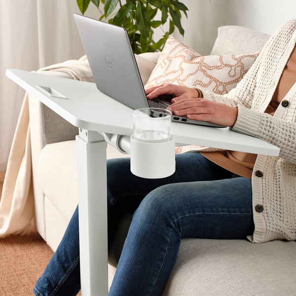 Person sitting on a couch using a height-adjustable laptop table with a cup holder.