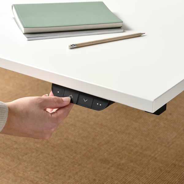 Person adjusting sit/stand desk control panel under white table.