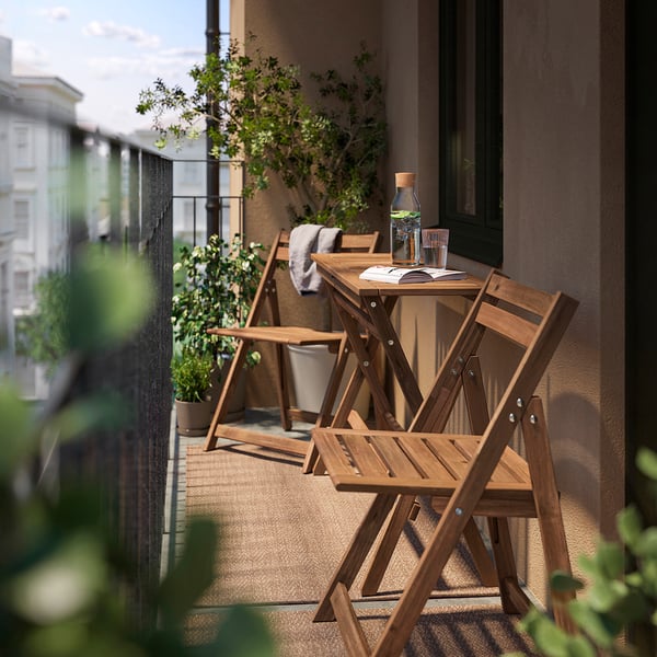 Small balcony with wooden table and chairs, green plants, and city view.