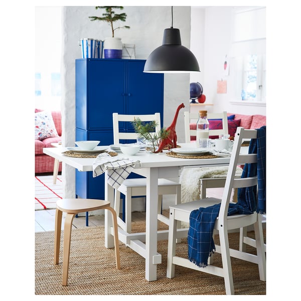 Bright dining area with white table, chairs, blue cabinet, red dinosaur, black lamp.