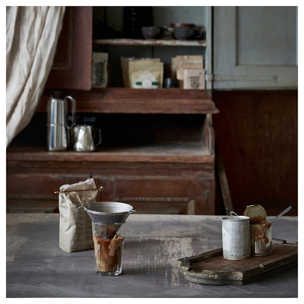 Vintage kitchen with coffee setup, including a silver coffee philtre, bagged beans, and containers with utensils on a rustic wooden table.