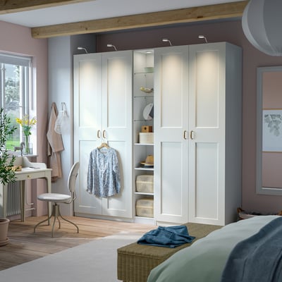 Modern bedroom with narrow PAX wardrobe in white, featuring glass and wooden shelves for storage and display.