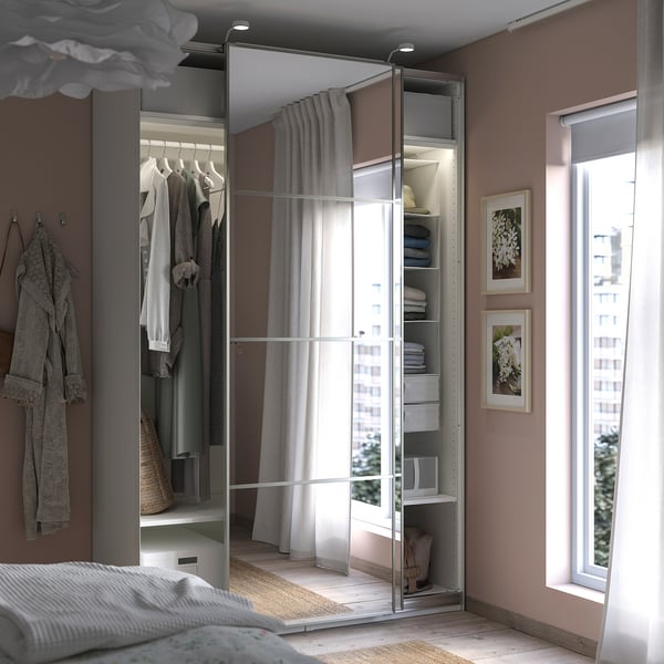 Modern bedroom with PAX mirrored wardrobe. Its creme-white, has sliding doors, and houses clothes, with a window beside it.