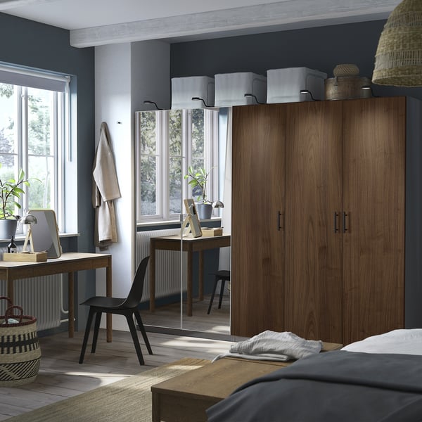 Spacious bedroom with large PAX wardrobe in dark wood, black chair, and wooden desk near window. Room decorated with simple, modern design.