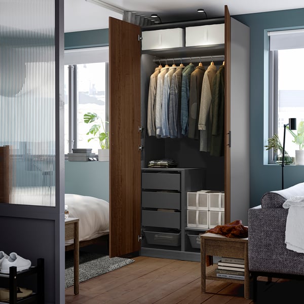 Open wardrobe with hanging shirts, drawers, and storage boxes, set in a bedroom with wooden floors and blue walls.