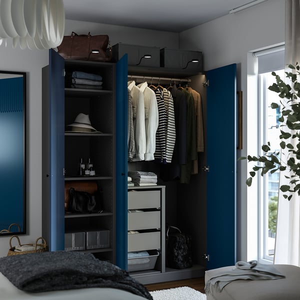 Open blue PAX wardrobe showing clothes, shelves with folded items, and drawers. Hats and bags are stored neatly.