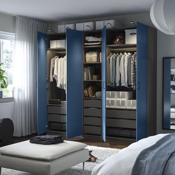 Bedroom with blue PAX wardrobe open, showing shelves, drawers, and clothes.