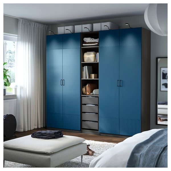Blue PAX wardrobe in modern bedroom, tall beside window, with drawers and shelves.