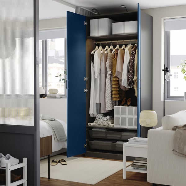 Open blue PAX wardrobe reveals clothes hangers, storage boxes, and shelves in a neat bedroom setting.