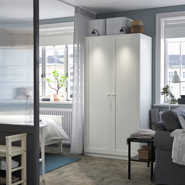 Modern room with white PAX wardrobe, tall and narrow, fitting between windows. Grey couch and blue rug, grey walls.