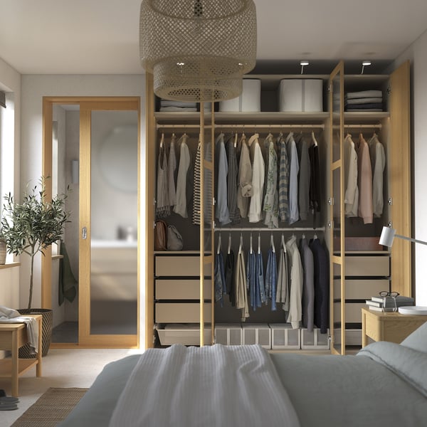 A modern bedroom with a blue bed and wooden wardrobe. Neatly organised clothes and a stylish pendant light hang above.