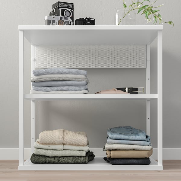 White PLATSA shelf unit with folded clothes, camera display, and plant.