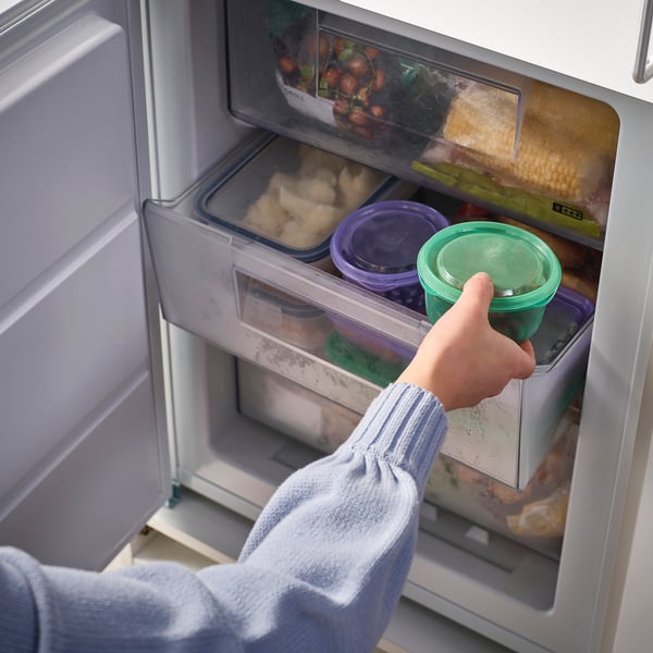 Person grabbing green container from fridge, storing leftovers or snacks, ideal for school or work lunches.