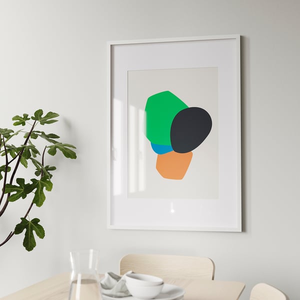 Abstract art in white frame on light wall above dining table.