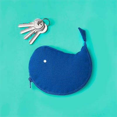 Blue whale-shaped key pouch on turquoise. Holds small items, metal zip, compact size.