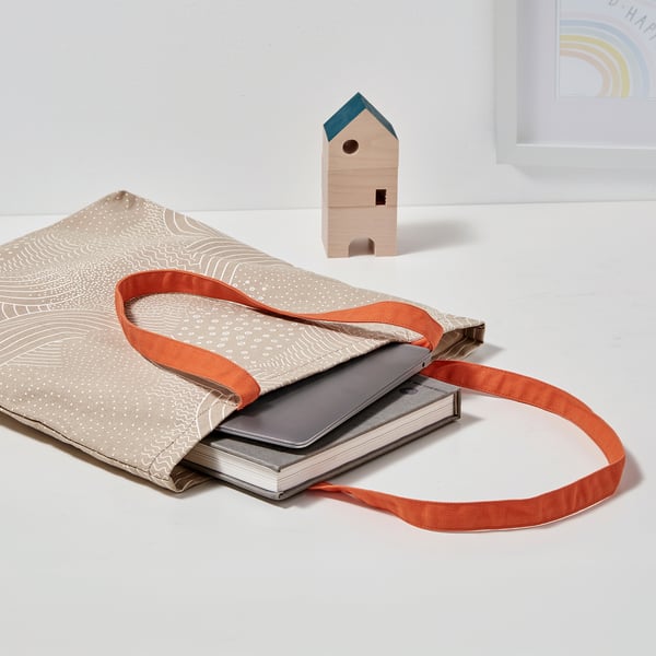 Beige tote bag with orange handles, white pattern, for laptop & papers.