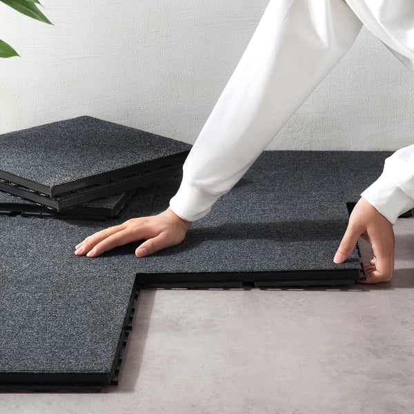 Person assembling RUNNEN floor tiles, demonstrating easy click-together setup for a soft, comfortable outdoor surface.