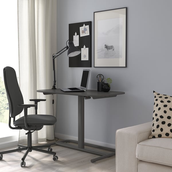 Modern home office with SEGRARE sit/stand desk, black chair, laptop, tablet, zebra art, and beige armchair.