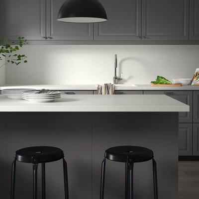 Modern kitchen counters with contrasting light and dark tones; black round stools neatly positioned; clean plates and utensils on the counter.