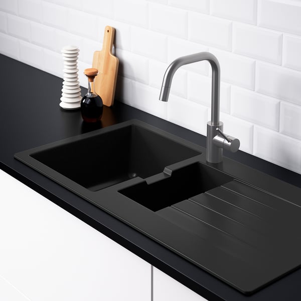 Modern kitchen sink with integrated drainboard. Silver faucet, black countertop, and white-tiled wall.