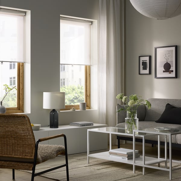 Modern living room with SKOGSKLÖVER cordless blinds, white sofa, wicker chair, coffee table & lamp.