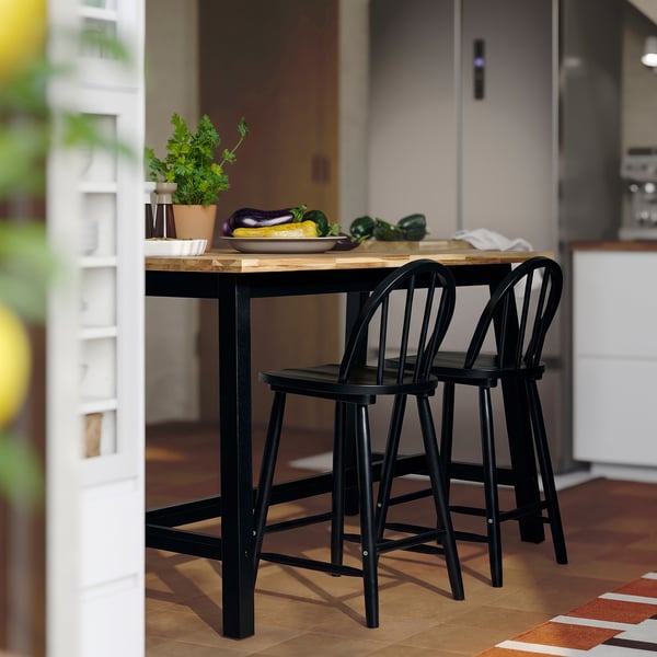 Small black wooden kitchen table with two chairs, set near a white door. Fresh vegetables and herbs on table.