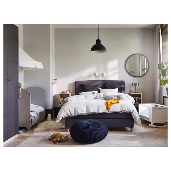 A modern bedroom with a SKURUP black pendant lamp, a grey bed, and a white cribs.