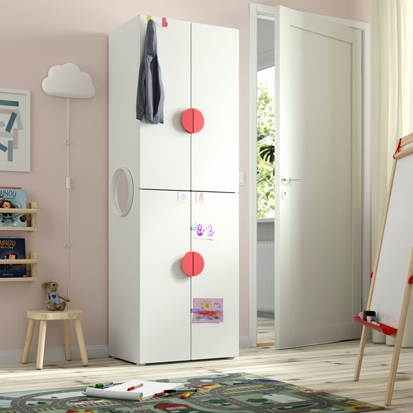 Kids room with white SMÅSTAD wardrobe, pink walls, bookshelf, teddy bear, toy ladder. Wardrobe stands tall near door.