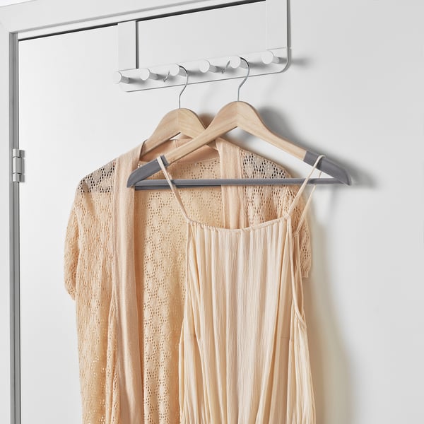 A beige lace dress hangs on a wooden hanger with flocked surface to prevent sliding, suspended from a chrome hook on a white wall.