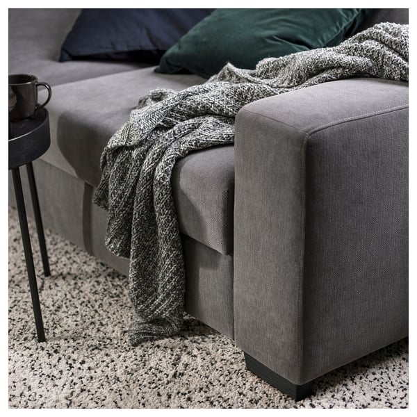 Cosy modern grey sofa with knit blanket and pillow, black side table with cup.