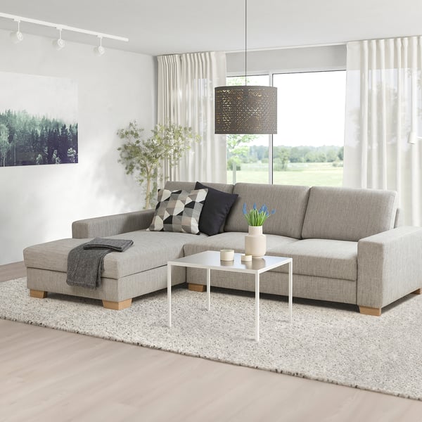 Modern living room with grey sofa, pillows, coffee table, plant, rug, and large windows.