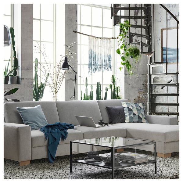 Modern, minimalist living room with large windows, grey SÖRVALLEN sofa, glass coffee table, and various green plants.