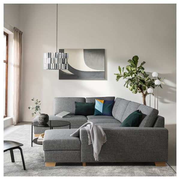 Modern living room with a large grey SÖRVALLEN sectional sofa, colourful pillows, a glass coffee table, and a stylish pendant lamp.